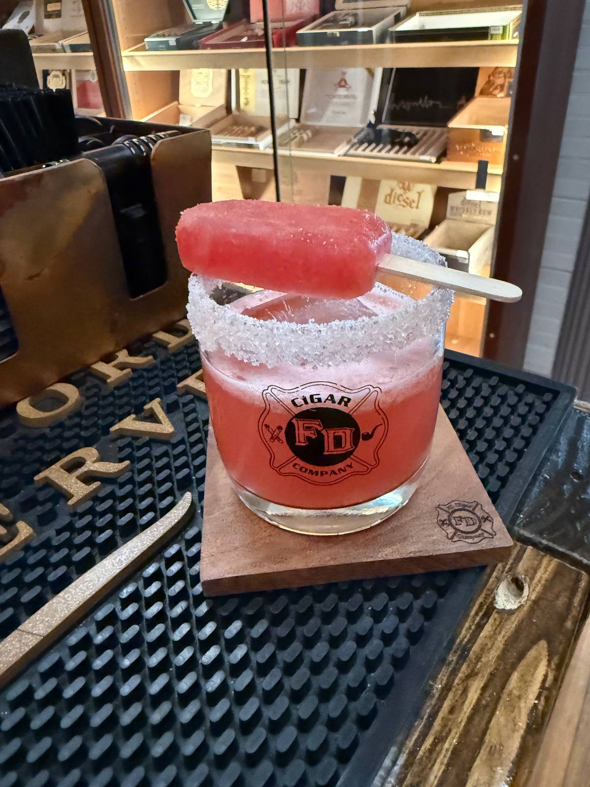 Watermelon Cucumber Sour in a sugar-rimmed FD Cigar Company rocks glass, topped with a watermelon popsicle garnish